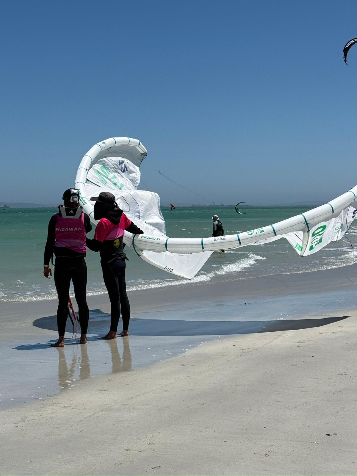 Two Obsession Kiting instructors carrying a wing along the beach at Langebaan